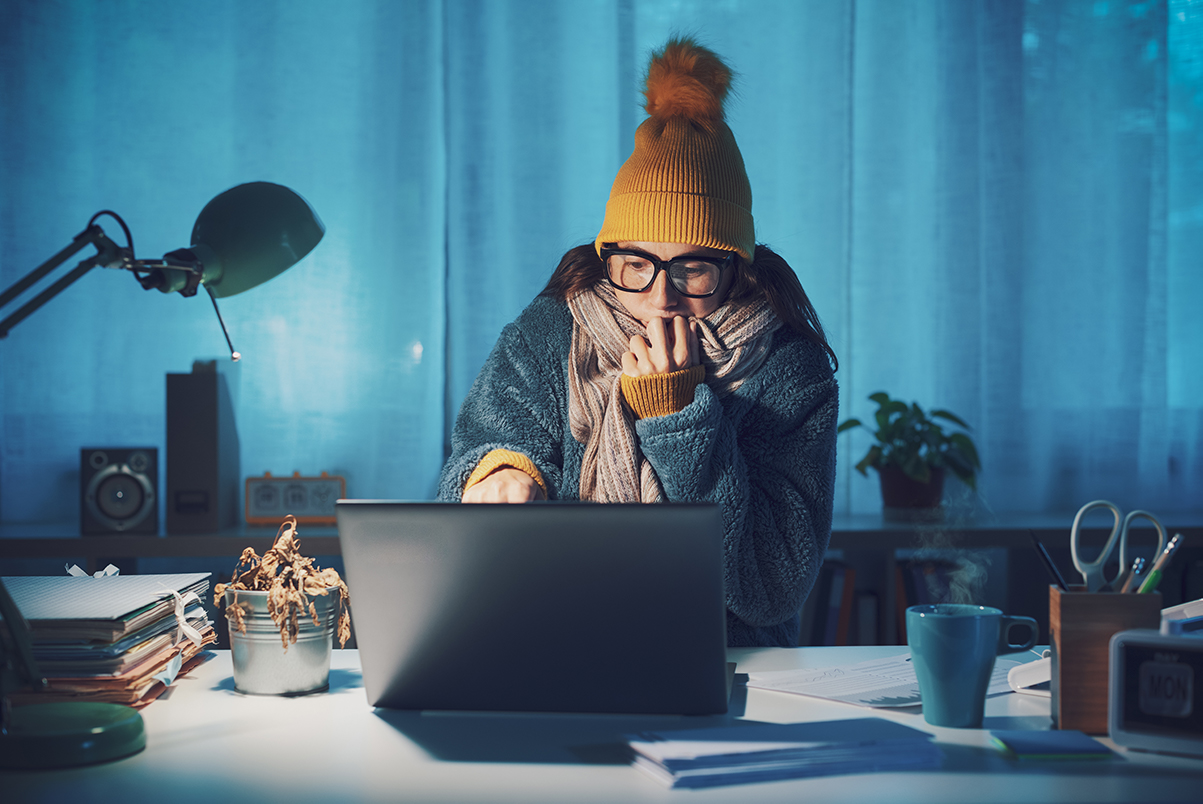 woman inside wearing cold weather clothing, bundled up, on laptop