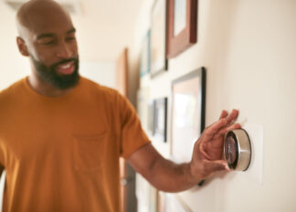 A smiling man adjusts his home heat pump’s thermostat.