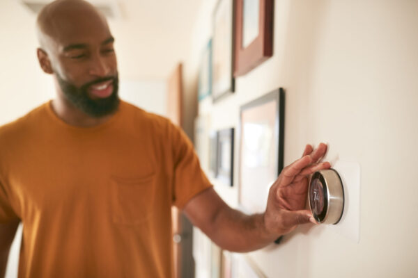 A smiling man adjusts his home heat pump’s thermostat.