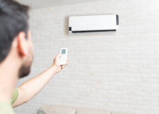 Mid adult man adjusting temperature of air conditioner using remote control at home